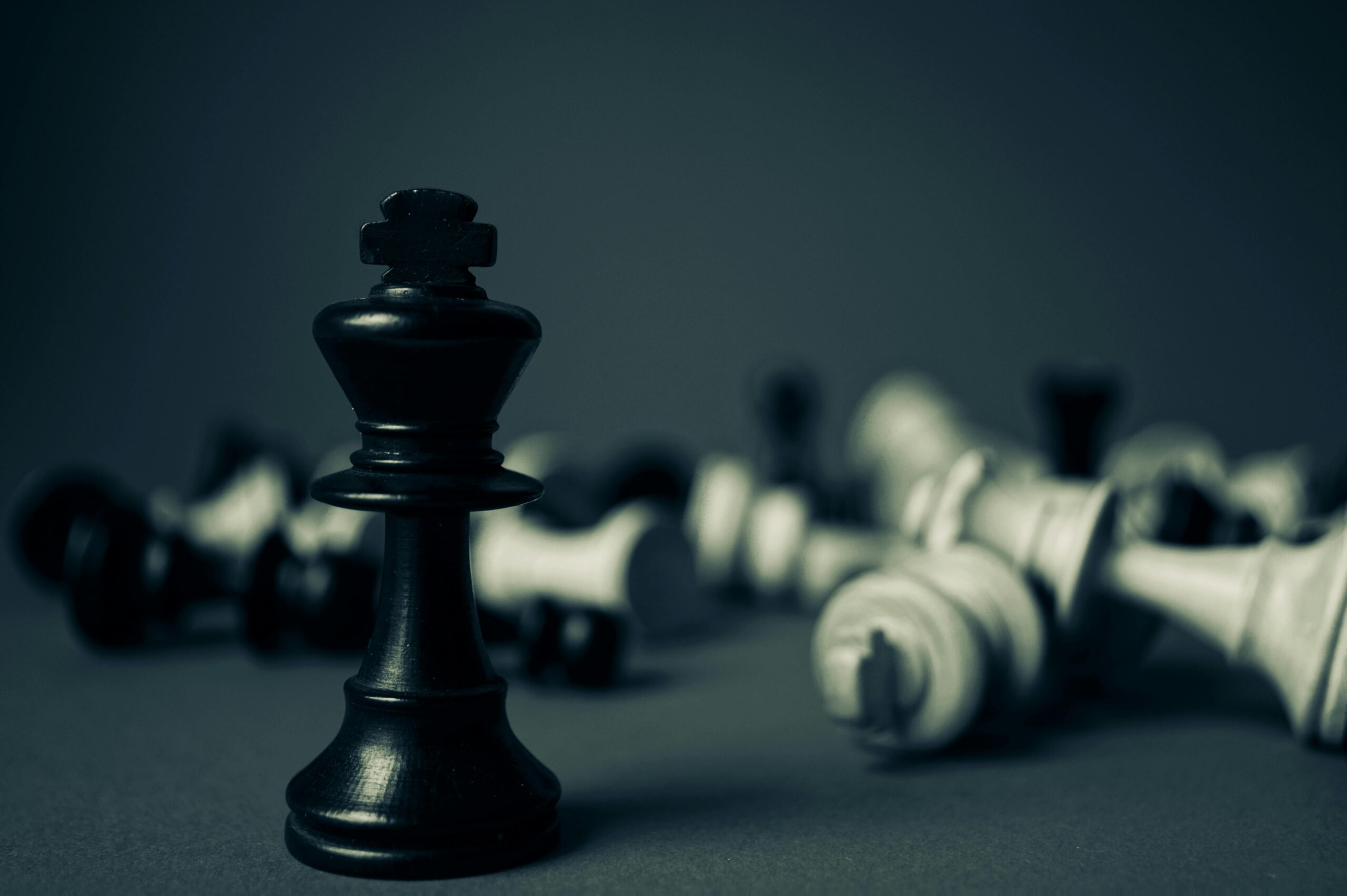 Black king chess piece stands tall among fallen pieces, symbolizing strategy and triumph.
