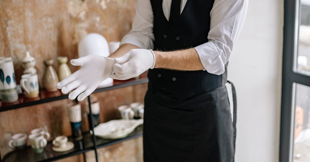Elegant waiter dressing up indoors, putting on white gloves before service.